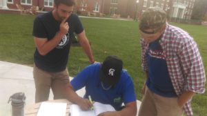 Junior member Aaron Botts and sophomore member Will McClure assist sophomore member Eder Sosa with his homework in back circle.